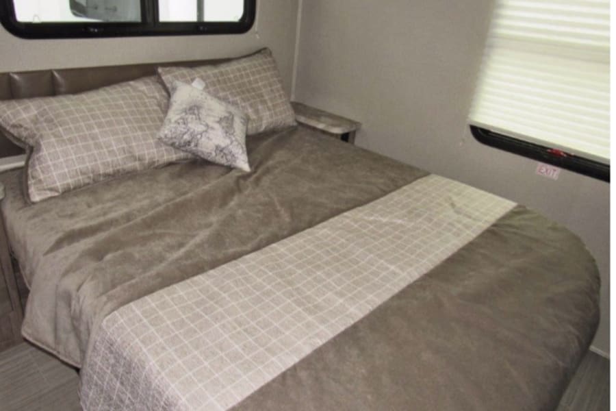 A spacious RV rental bedroom featuring a large bed with neutral bedding, a headboard, and an emergency exit window.