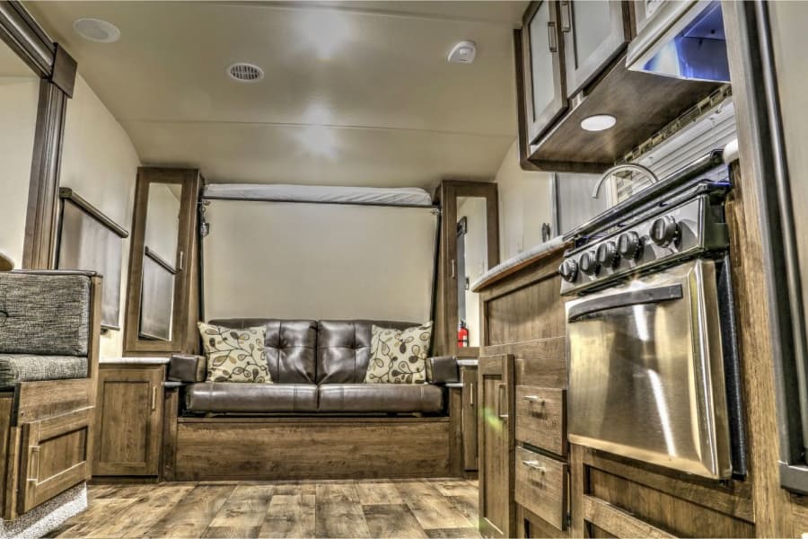 Spacious RV rental interior featuring a versatile sofa, pull-down bed, and compact kitchen area for comfortable travel.