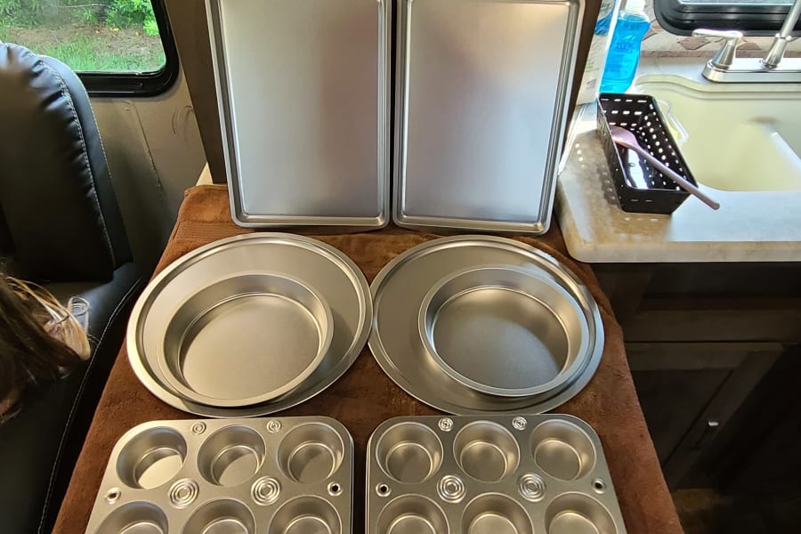 Various silver baking pans (sheet, round, muffin) inside an RV rental, prepped for cooking in a compact kitchen.