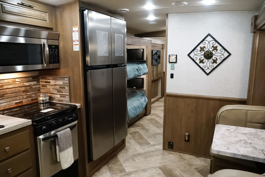 Inside an RV rental: a modern kitchen with stainless appliances, bunk beds with TVs, and a cozy dining booth.