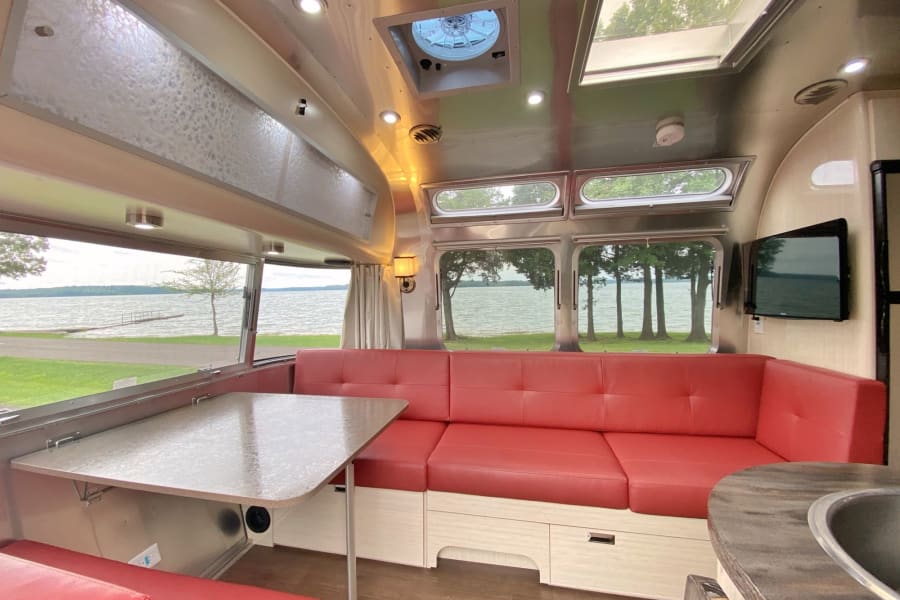 Inside this Airstream RV rental: a bright living space with red dinette seating and panoramic lake views. Perfect camper stay.