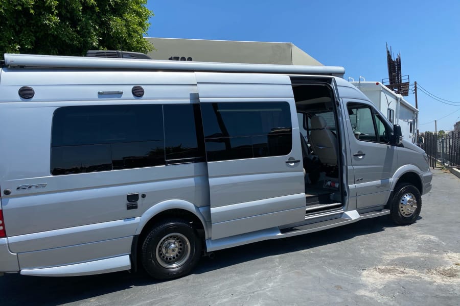Silver Mercedes Sprinter RV rental: a modern camper van with open side door and extended awning for your travels.