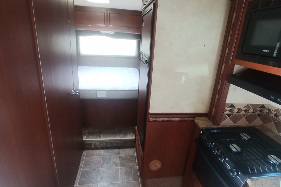 RV rental: View inside, showcasing a compact kitchen with stove & microwave, and a bedroom area to the left.