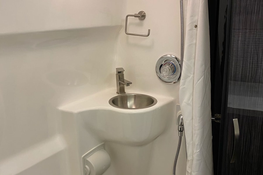 This RV rental wet bath features a compact shower, stainless sink, toilet, and adjustable showerhead, optimizing small spaces.