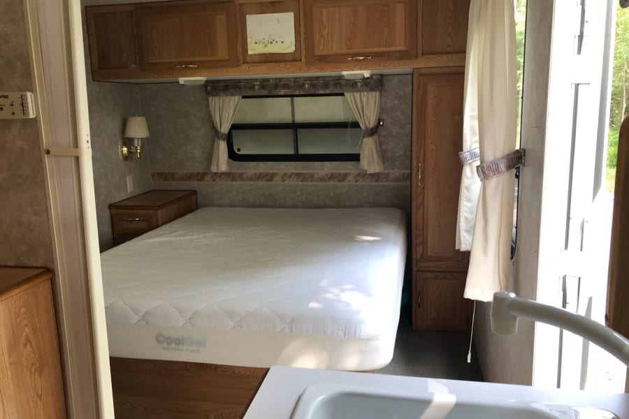 RV rental bedroom view: large mattress, wood cabinets, and window with curtains. Ideal for mobile living and travel.