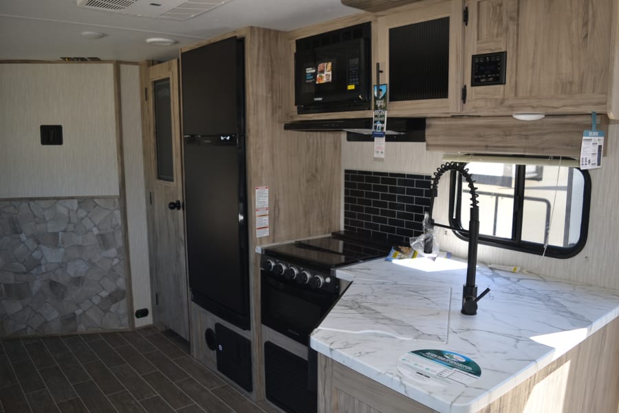 Spacious RV rental interior featuring a modern kitchen with black appliances, white marble-look counters, and wood flooring.