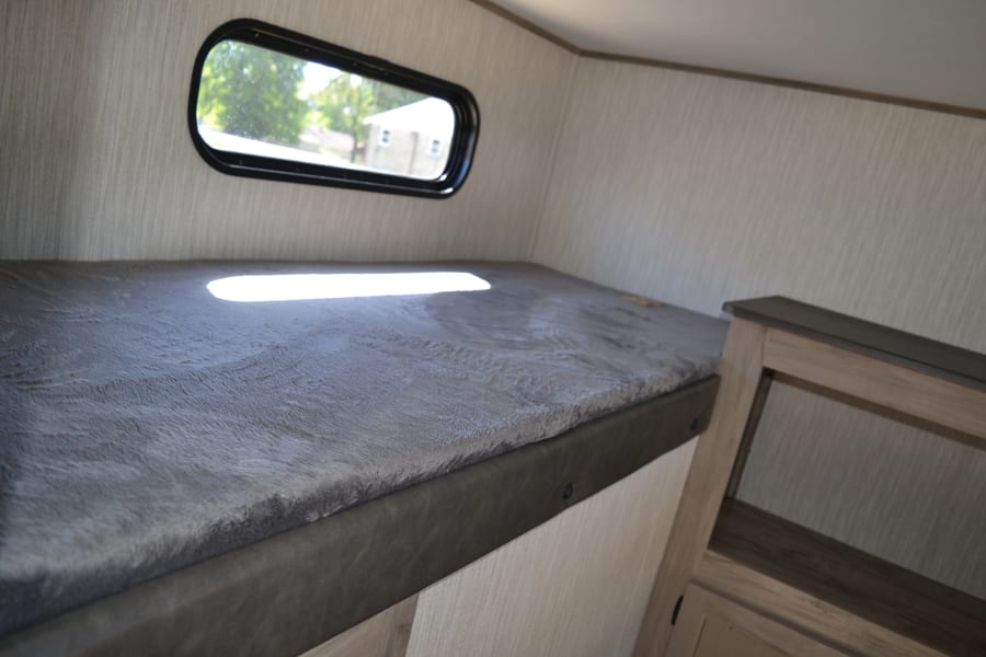 Cozy RV rental bunk bed interior, featuring a window and plush mattress. Ideal for compact travel adventures.