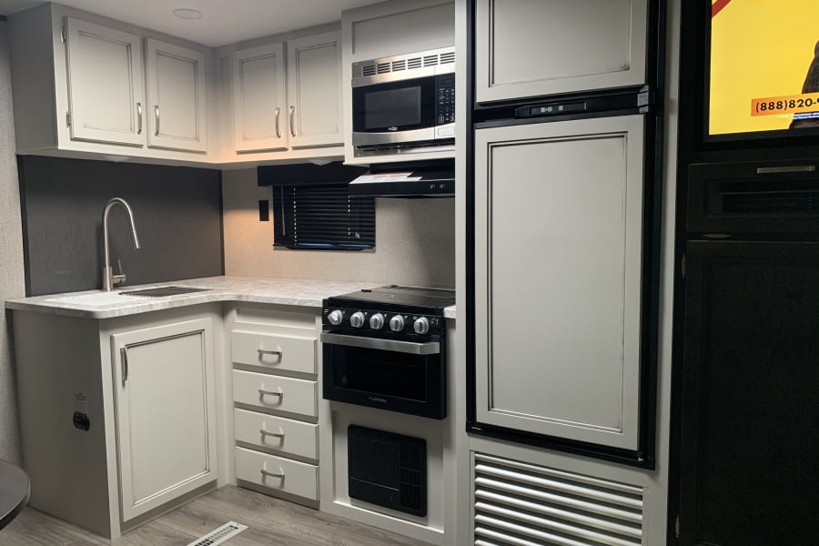 This RV rental's modern kitchen includes a sink, stove, microwave, and refrigerator, providing essential amenities for travel.