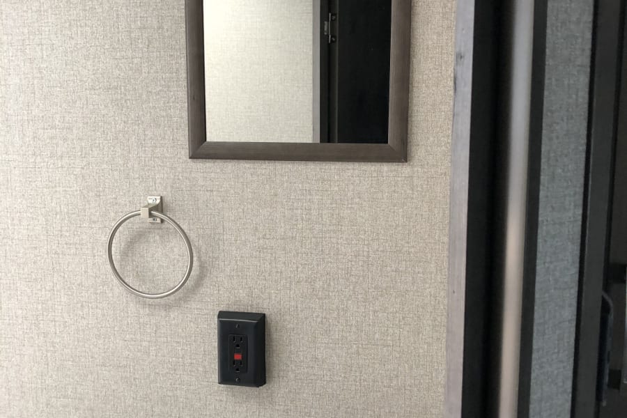 Inside an RV rental bathroom, featuring a mirror, towel ring, sink with faucet, and GFCI outlet on textured walls.
