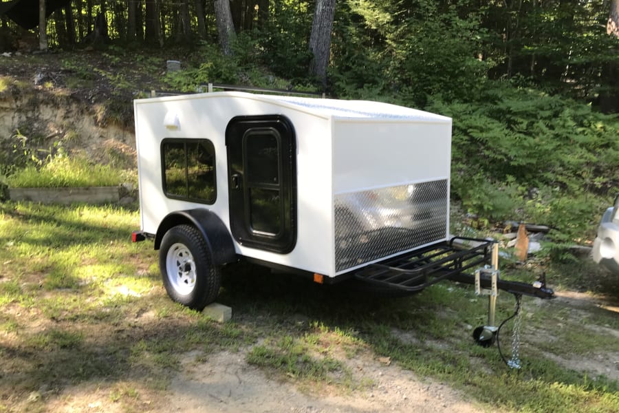 Experience nature with this white compact travel trailer. Perfect for an RV rental, it features a side door, window, and front rack.