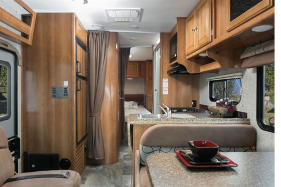 RV rental interior: practical living space with a kitchen, dining area, and rear bedroom. Wood finishes and functional design.