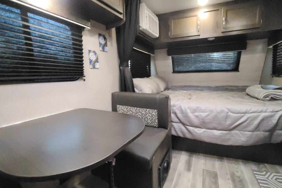 RV rental interior featuring a compact dining area, comfortable bed, and overhead storage cabinets.