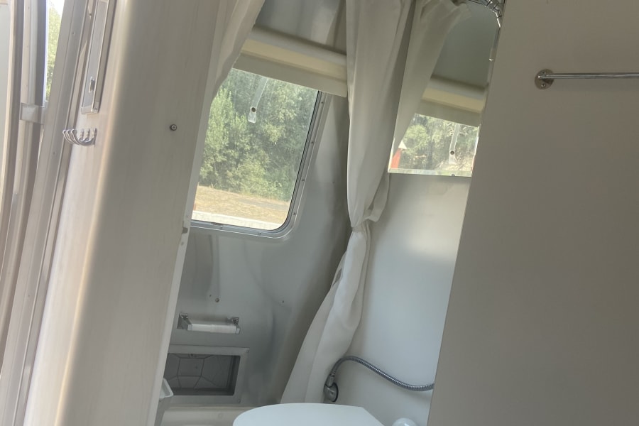 Interior of an RV rental: a bright, compact bathroom featuring a white toilet, shower, and windows for natural light.