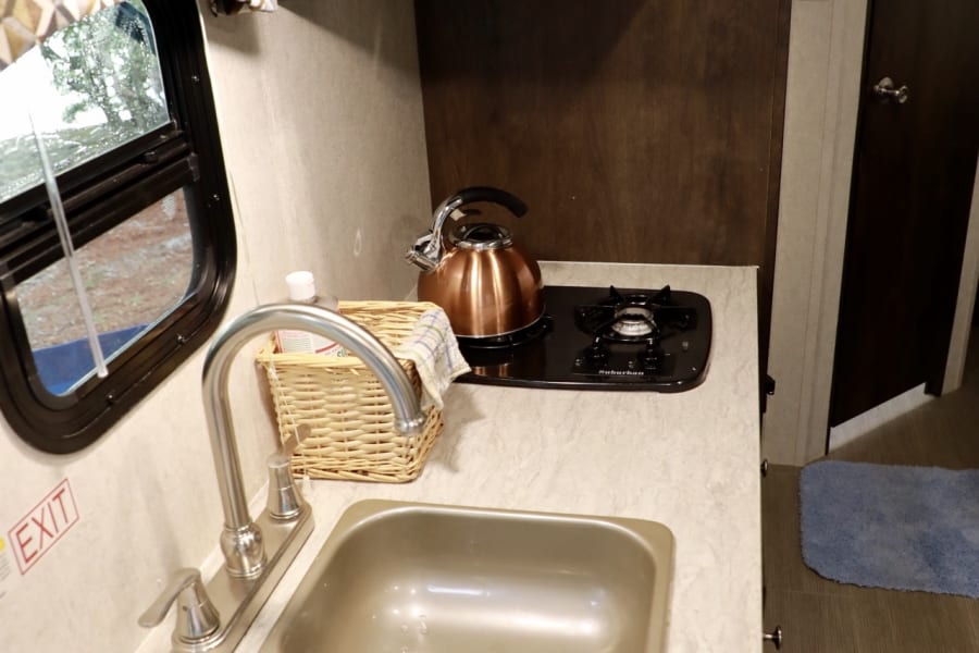 Explore this RV rental's practical kitchenette with a sink, two-burner stove, and kettle, showcasing its compact interior.