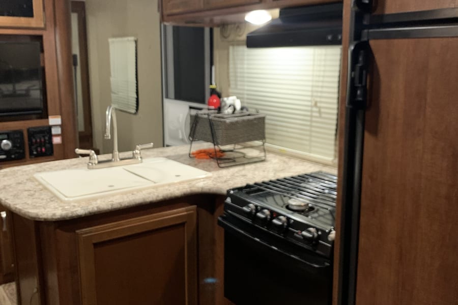 Compact RV rental kitchen with sink, stove, microwave, and wood cabinets, offering efficient space utilization.