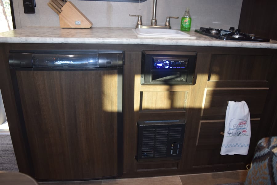 Compact RV rental kitchen area features Dometic fridge, sink, stove, and integrated stereo, providing travel comforts.