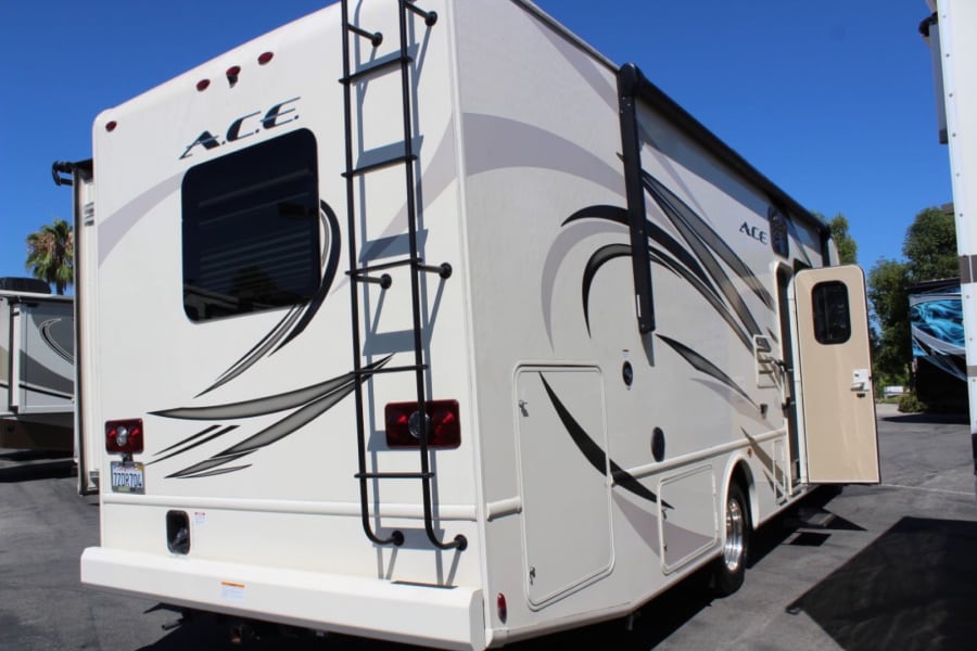 Spacious cream-colored ACE motorhome, featuring a rear ladder, side awning, and open entry, awaits your next rv rental adventure.