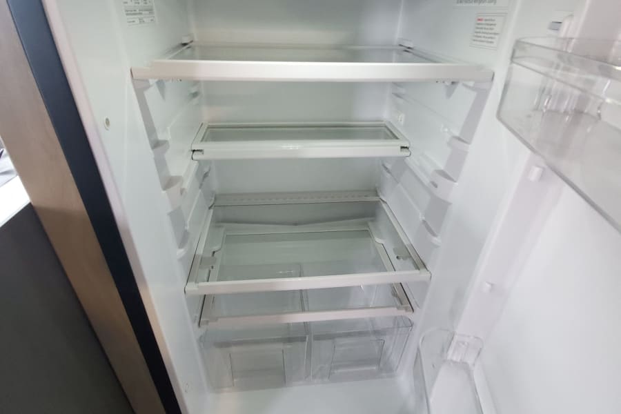 Inside a spotless RV rental refrigerator: empty shelves, bright light, and clear bins. Ready for your trip!