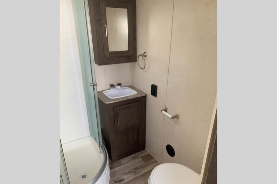 Compact RV rental bathroom featuring a shower, sink vanity, toilet, and medicine cabinet, perfect for travel.
