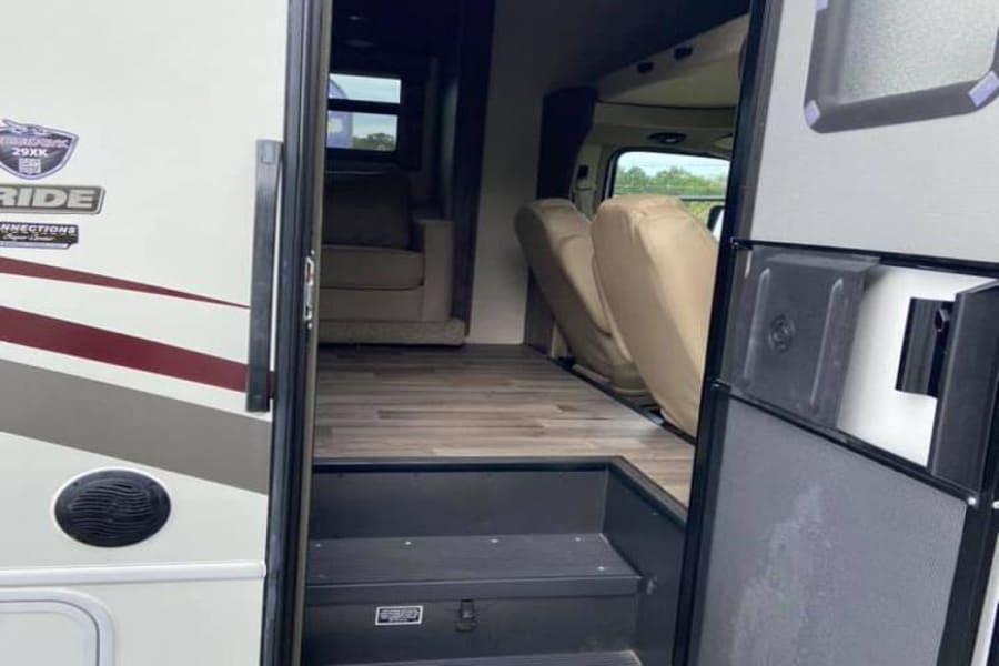 RV rental interior view: open door, steps, wood floor, living area, and front seats are visible inside this spacious vehicle.