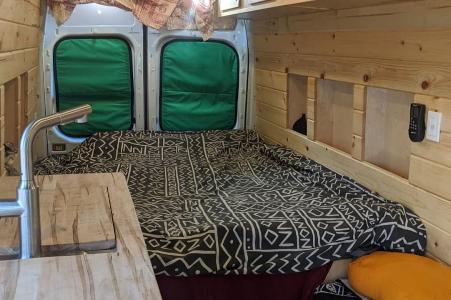 This RV rental's wood-paneled interior features a cozy bed, kitchen sink, and clever storage options for van life.