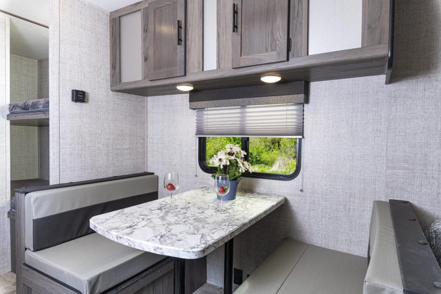 RV rental interior showcasing a dinette with marble table, seating, overhead cabinets, and built-in bunk beds.