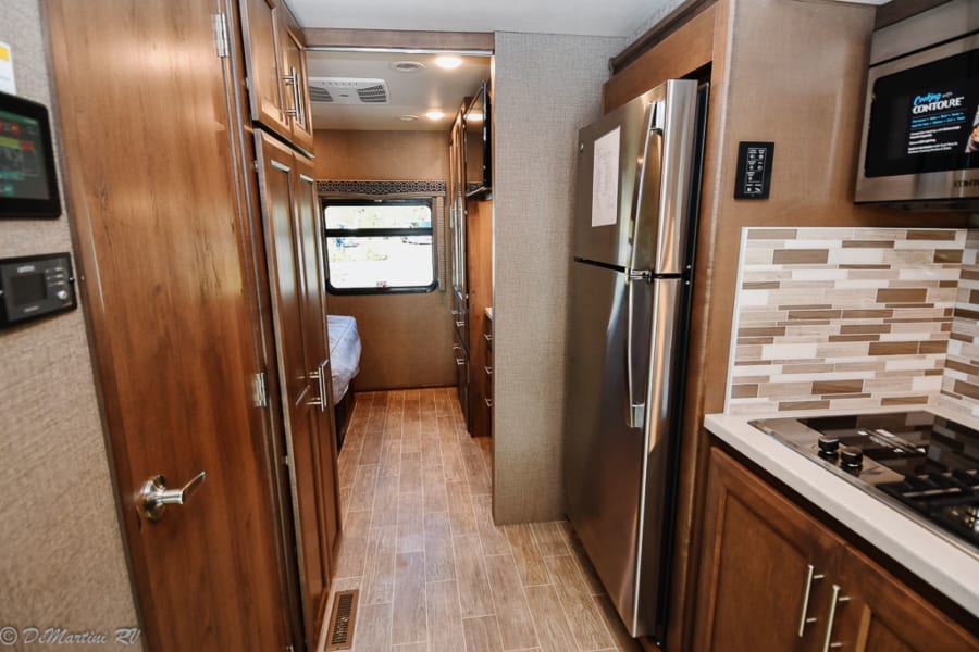 RV rental interior: compact kitchen with stainless appliances, leading to a cozy bedroom.