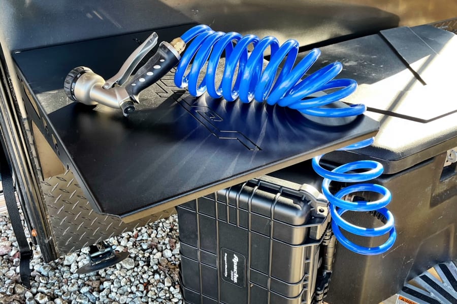 RV rental ready: A blue coiled hose and nozzle on a black outdoor shelf with a storage case.