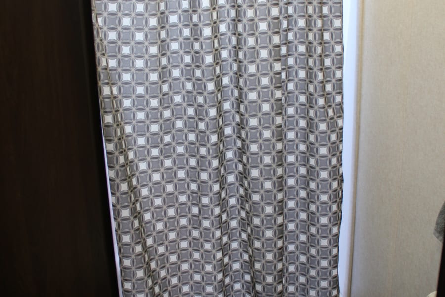 Compact RV rental bathroom: features a white toilet, geometric shower curtain, and wood-look floor.