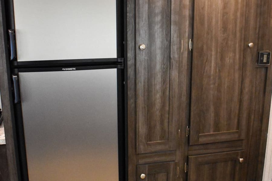 RV rental interior with a Dometic two-door refrigerator and built-in dark wood-grain storage cabinets, providing essential space.