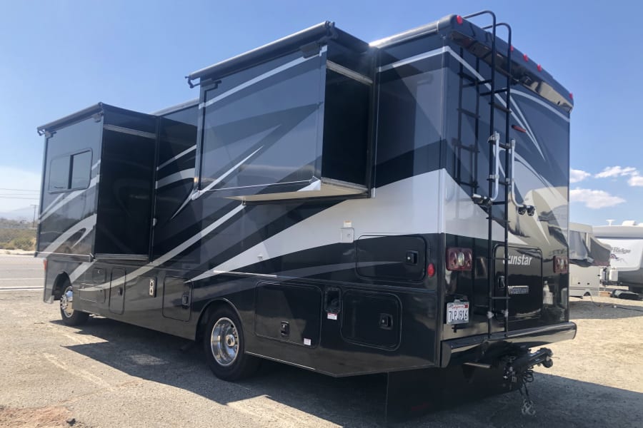 Spacious black and white Winnebago Sunstar rv rental with slide-outs extended, parked outdoors.