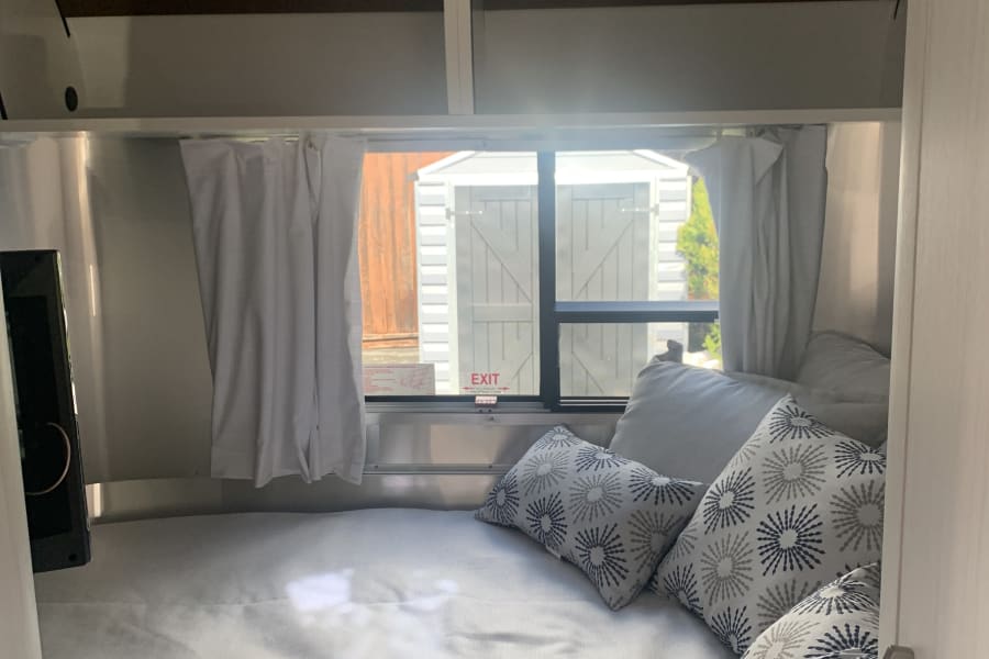 RV rental cozy sleeping area: bed with sunburst pillows, TV, overhead storage, and a bright window.