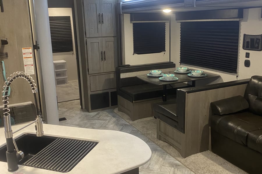 Inside this RV rental: a modern kitchen with sink, cozy dining booth with bowls, and a plush sofa for comfortable living.