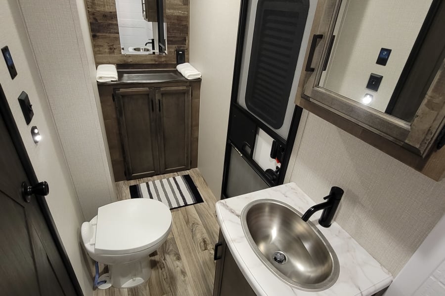 Compact RV rental bathroom with modern sink, toilet, mirror, and shower. Perfect for travel!
