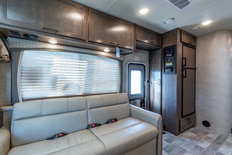 Inside an RV rental: comfy sofa, overhead cabinets, and fridge in a cozy living space, ideal for road trips.
