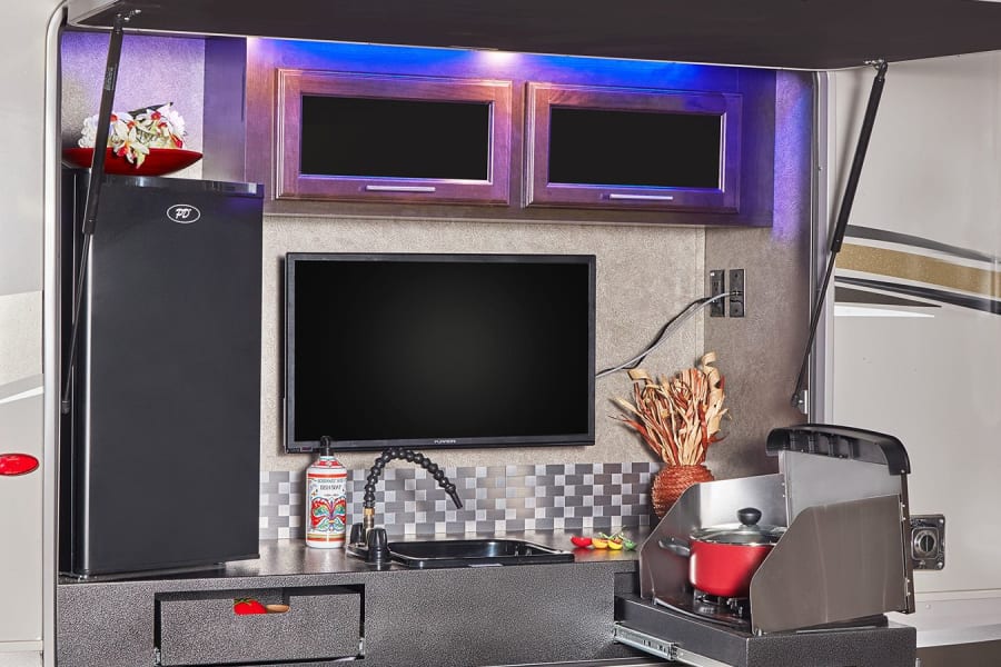 This RV rental features a full outdoor kitchen: fridge, TV, sink, and pull-out stove, perfect for open-air cooking.