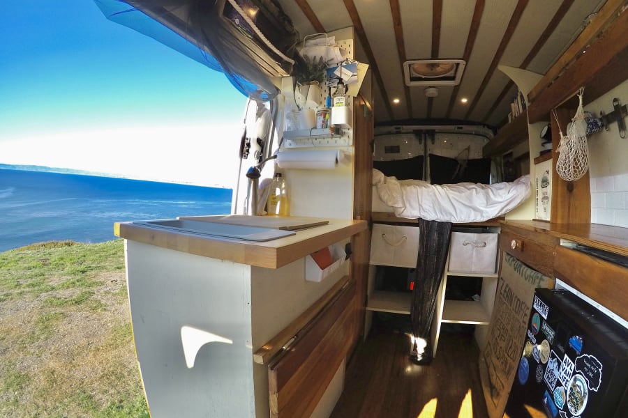Interior of an RV rental: a cozy camper van with a stunning ocean view from the open door, showcasing the ultimate van life experience.