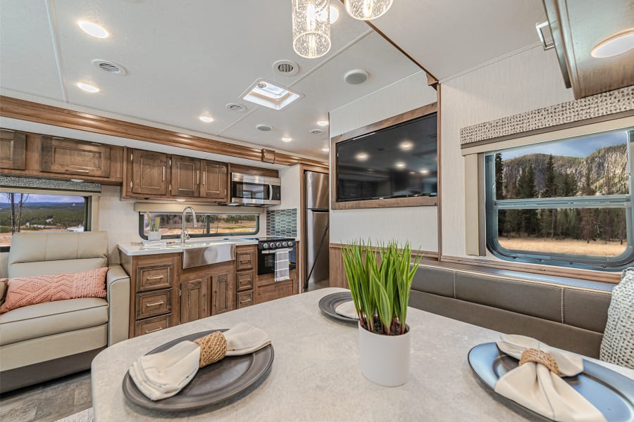 Spacious RV rental interior featuring a modern kitchen, dining area, comfortable seating, and scenic window views.