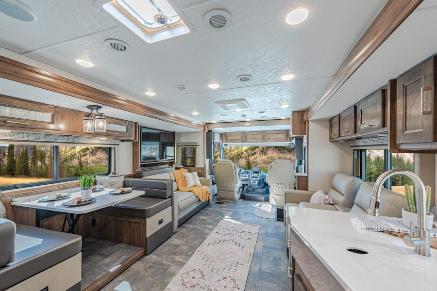 Inside a modern RV rental: a well-appointed living room, dining area, and kitchen setup, ideal for your next road trip.