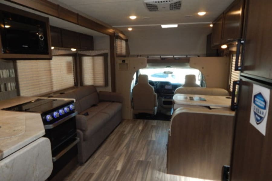Inside a spacious RV rental: modern kitchen, sofa, dinette, and driver's cab visible. Ready for your next adventure!