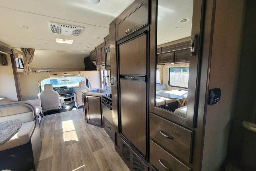 Step inside this modern RV rental! Features a full kitchen, dinette, and living area, with front cab visible.