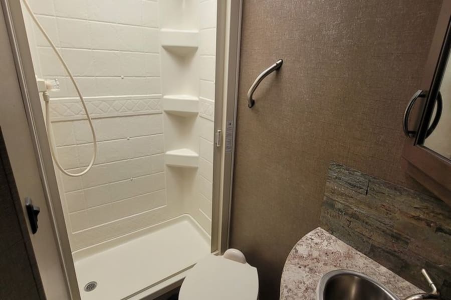 Explore this RV rental's compact bathroom, featuring a bright shower, toilet, and modern sink with stone accent backsplash.