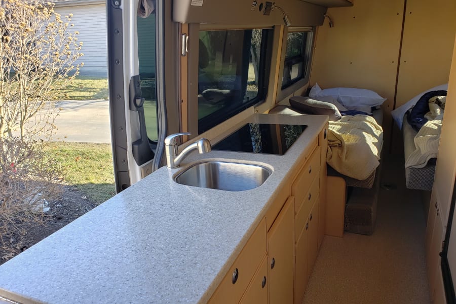 RV rental interior: compact kitchen with sink, induction cooktop, and two beds. Ready for your next adventure.