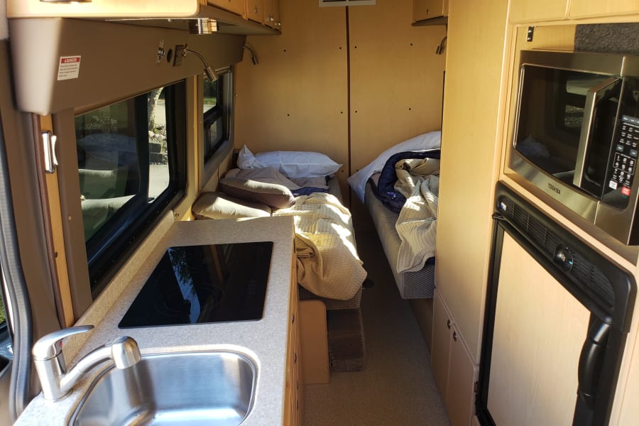 Compact RV rental interior featuring a kitchenette, twin beds, microwave, and fridge, perfect for travel adventures.