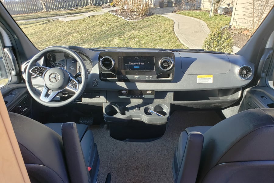Step into this Mercedes-Benz RV rental! A spacious cockpit features a modern dashboard, steering wheel, and front seats.