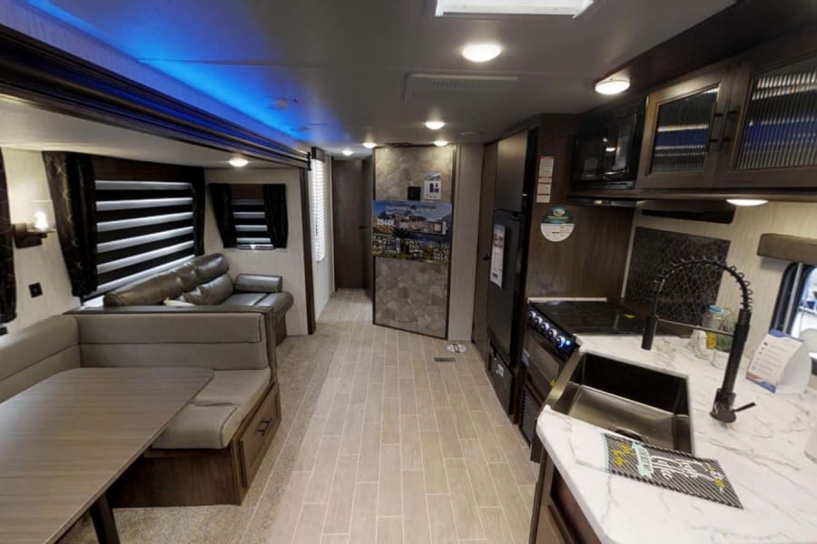 This RV rental interior showcases a modern kitchen, living space with dinette, and comfortable seating, ideal for travel.