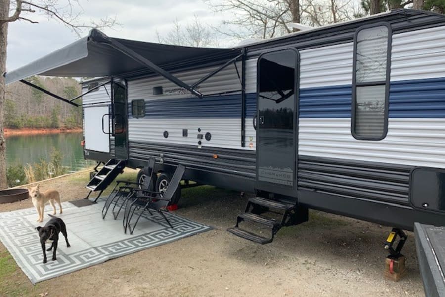 This RV rental offers a lakeside retreat with an extended awning, outdoor living space, and two dogs relaxing.