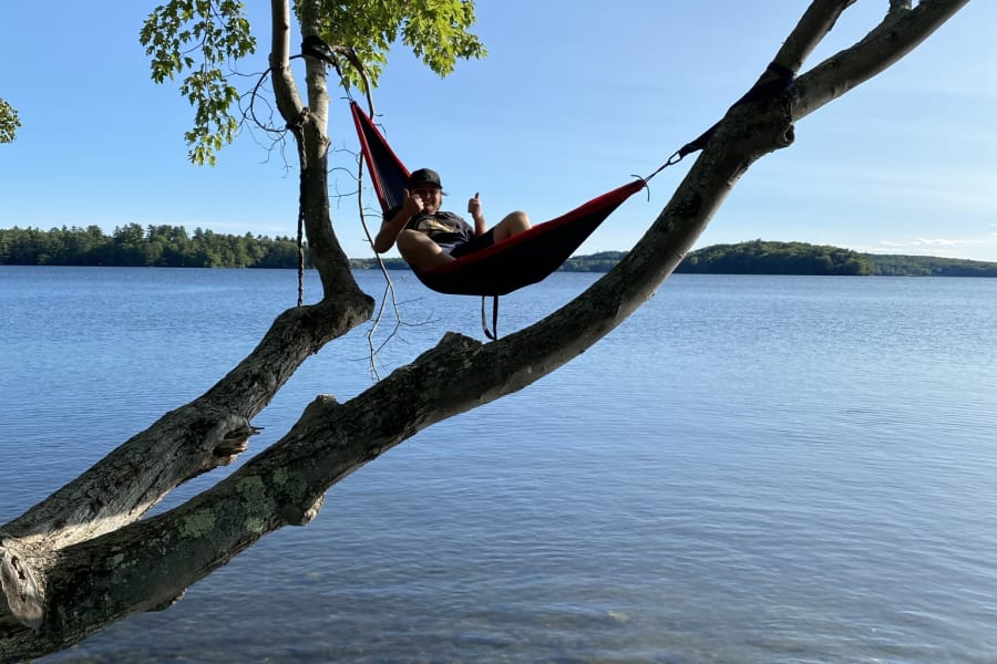 Relaxing in a hammock suspended over a serene lake, a happy person gives thumbs up. Ideal after an RV rental journey!