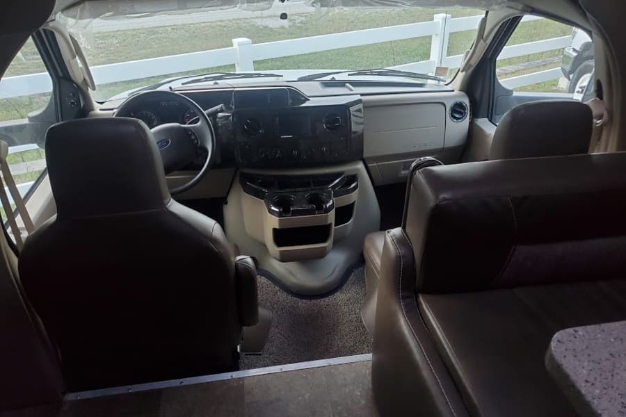 Step into this clean rv rental. View of the motorhome cockpit: driver/passenger seats, dashboard, and living area.
