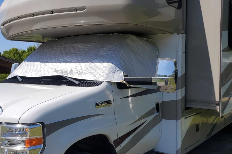 This white motorhome, equipped with a reflective windshield sunshade and side slide-out, is ready for an RV rental adventure.